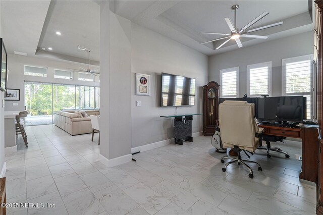 office space featuring a ceiling fan, a raised ceiling, healthy amount of natural light, baseboards, and recessed lighting