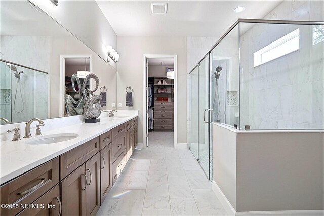 full bath featuring a stall shower, marble finish floors, a walk in closet, and double vanity