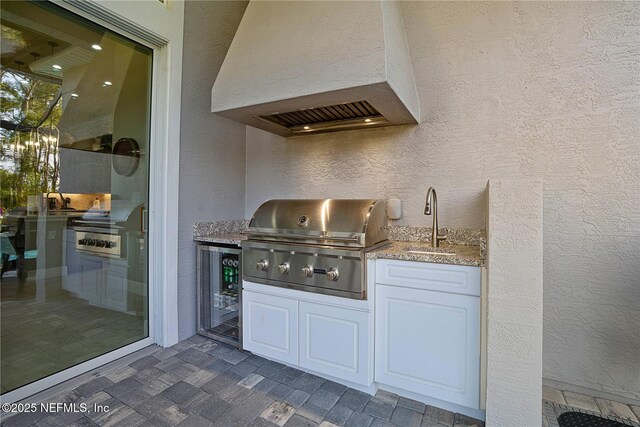 bar area featuring premium range hood, a sink, a textured wall, wine cooler, and a chandelier