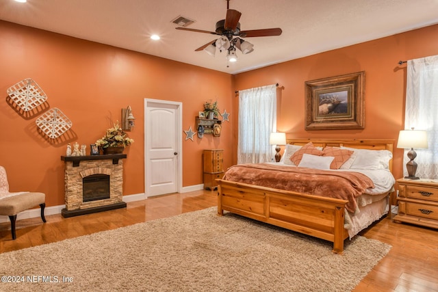 bedroom featuring wood finished floors, visible vents, baseboards, a stone fireplace, and recessed lighting