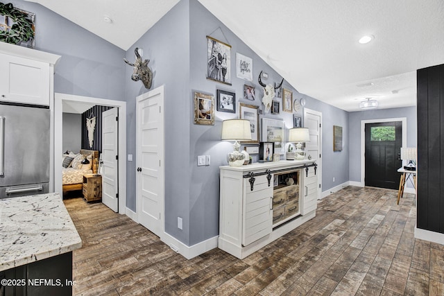 hallway with dark wood finished floors, lofted ceiling, baseboards, a textured ceiling, and recessed lighting