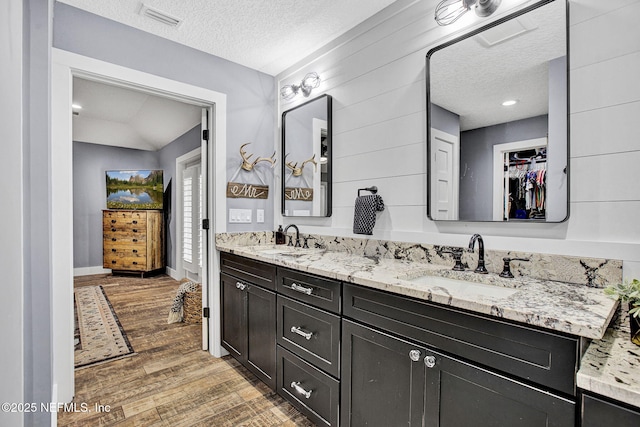 full bath featuring a textured ceiling, wood finished floors, baseboards, double vanity, and a spacious closet