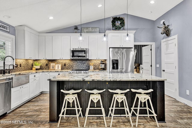 kitchen with appliances with stainless steel finishes, dark wood-style floors, a sink, lofted ceiling, and a kitchen island