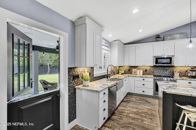 kitchen featuring stainless steel appliances, vaulted ceiling, white cabinets, light stone counters, and decorative backsplash