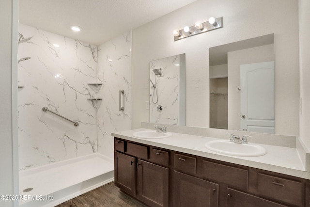 bathroom featuring a marble finish shower, double vanity, a sink, and wood finished floors