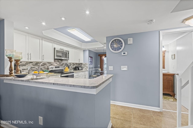 890 A1A Beach Blvd Unit 39, Saint Augustine, FL 32080 - kitchen with stainless steel appliances, a tray ceiling, tasteful backsplash, white cabinets, and a peninsula