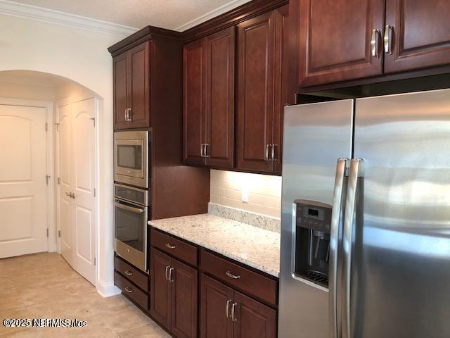 71 Utina Way, Saint Augustine, FL 32084 - kitchen with stainless steel appliances, crown molding, light stone countertops, arched walkways, and backsplash