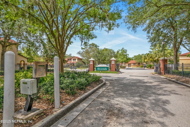 view of road featuring a gated entry, street lighting, and curbs