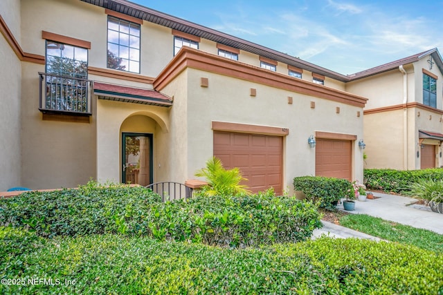 townhome / multi-family property with a balcony, stucco siding, and a garage