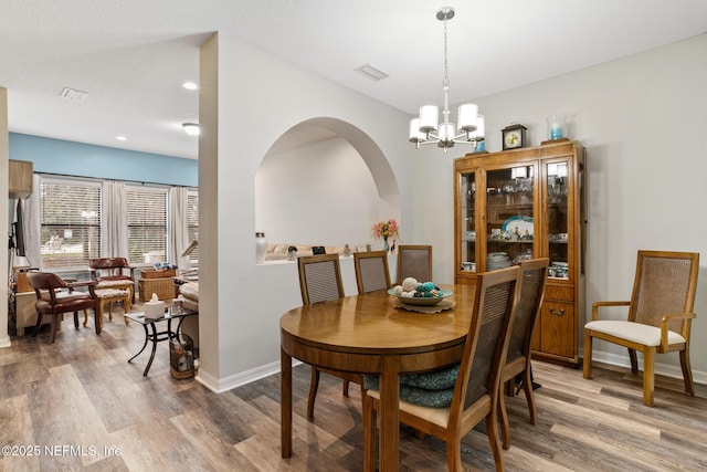 dining area with an inviting chandelier, light wood-style flooring, arched walkways, and baseboards