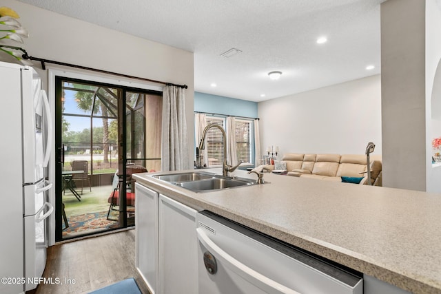 kitchen with light wood finished floors, light countertops, a sink, and white appliances
