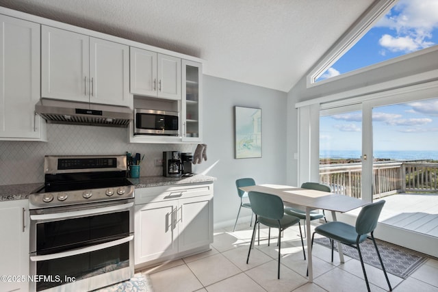 2122 S Fletcher Ave, Fernandina Beach, FL 32034 - kitchen with under cabinet range hood, light tile patterned flooring, vaulted ceiling, backsplash, and appliances with stainless steel finishes