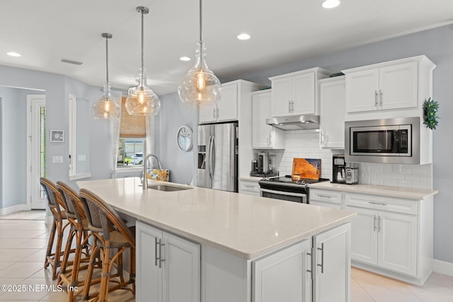 kitchen with recessed lighting, under cabinet range hood, light tile patterned floors, a sink, and appliances with stainless steel finishes