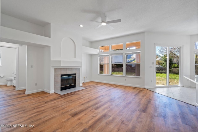 unfurnished living room with baseboards, a fireplace, ceiling fan, and wood finished floors