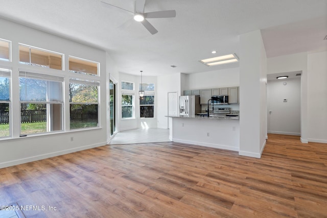 unfurnished living room with light wood-type flooring, baseboards, ceiling fan, and a sink