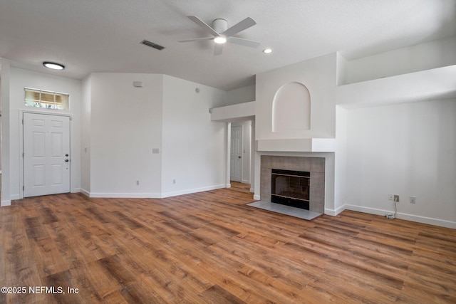 unfurnished living room with wood finished floors, visible vents, ceiling fan, baseboards, and a tile fireplace