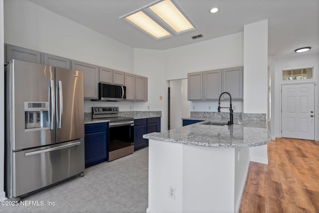 kitchen featuring a sink, a peninsula, stainless steel appliances, visible vents, and light stone countertops
