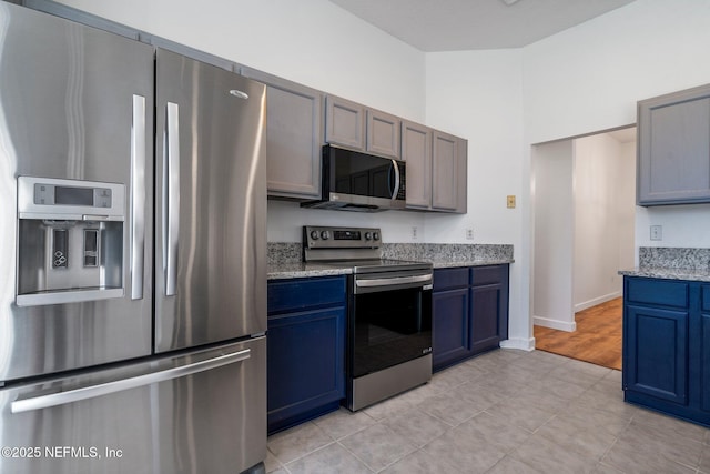 kitchen with appliances with stainless steel finishes, baseboards, light stone counters, and blue cabinets