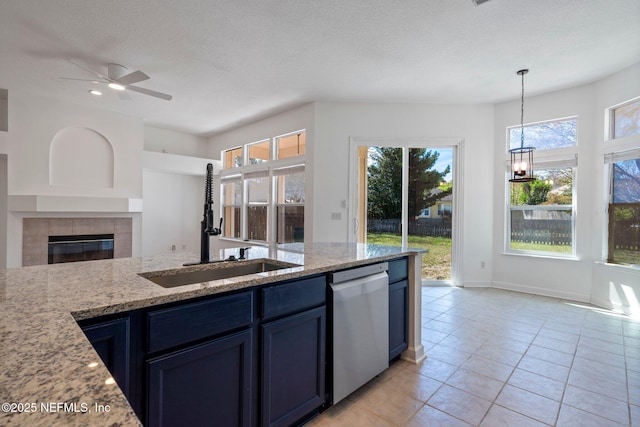 kitchen with a sink, a tiled fireplace, dishwasher, light stone counters, and blue cabinetry