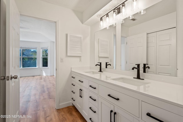 bathroom with baseboards, double vanity, a sink, and wood finished floors