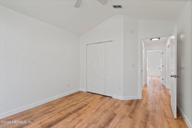 unfurnished bedroom with lofted ceiling, a closet, visible vents, baseboards, and light wood-style floors