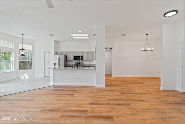 unfurnished living room featuring baseboards, light wood-style flooring, and ceiling fan with notable chandelier