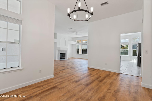 unfurnished living room with baseboards, visible vents, ceiling fan with notable chandelier, wood finished floors, and a fireplace