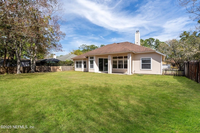 rear view of house with a yard, a chimney, and a fenced backyard