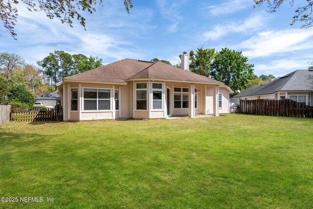 rear view of property with a shingled roof, a yard, a chimney, and fence