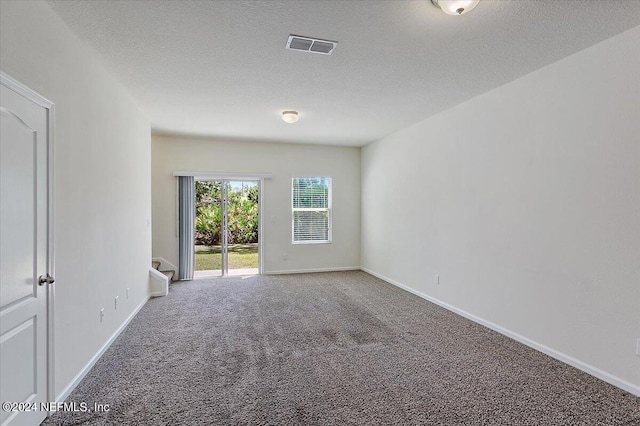 carpeted spare room featuring a textured ceiling, visible vents, baseboards, and stairs