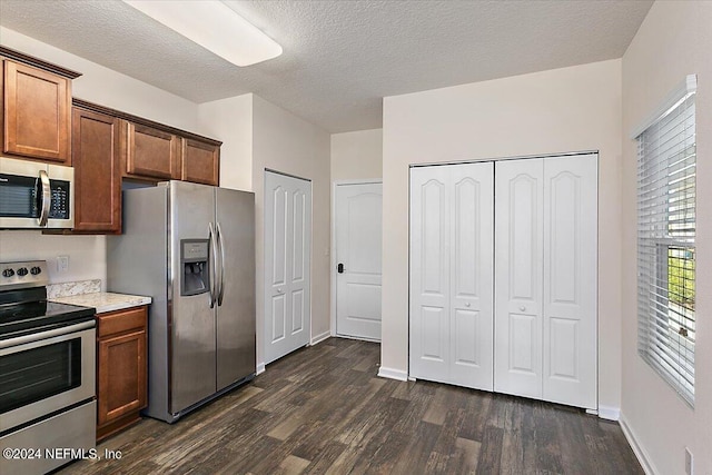 kitchen with a textured ceiling, baseboards, light countertops, appliances with stainless steel finishes, and dark wood-style floors