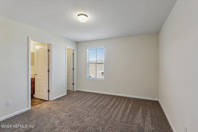 unfurnished bedroom featuring a textured ceiling, dark colored carpet, and baseboards