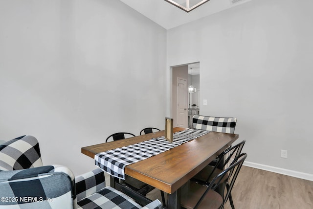 dining room with light wood-type flooring, visible vents, baseboards, and a high ceiling