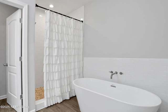 full bath with a soaking tub, tile walls, wood finished floors, and a tile shower