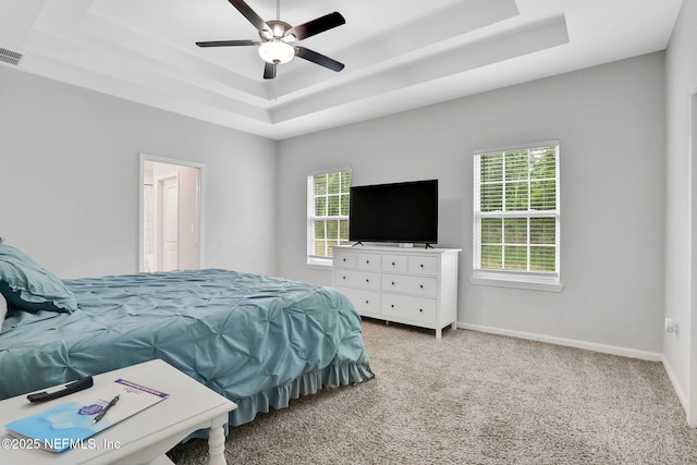 bedroom with a tray ceiling, light colored carpet, visible vents, and multiple windows
