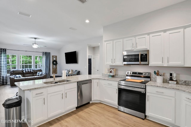 kitchen with a peninsula, appliances with stainless steel finishes, open floor plan, and a sink