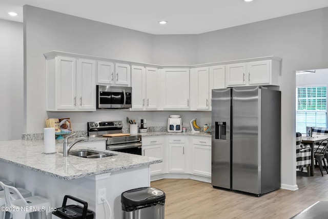 kitchen featuring a sink, a peninsula, white cabinetry, and appliances with stainless steel finishes