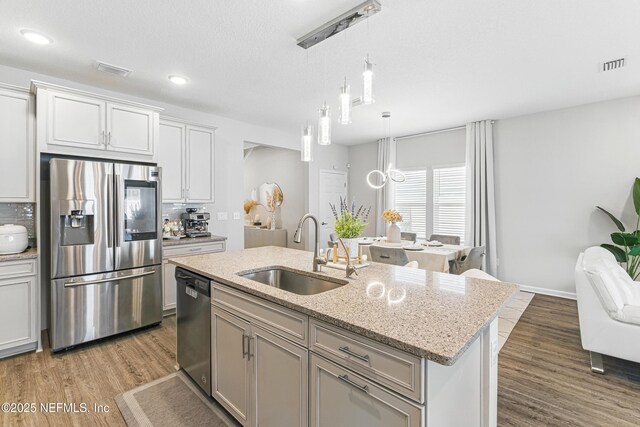 437 Narrowleaf Dr, Saint Johns, FL 32259 - kitchen featuring stainless steel appliances, a sink, wood finished floors, hanging light fixtures, and light stone counters