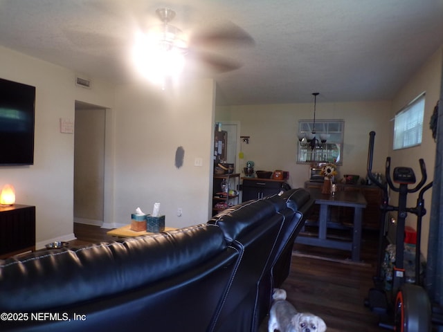 living area featuring ceiling fan with notable chandelier, visible vents, a wood stove, and wood finished floors