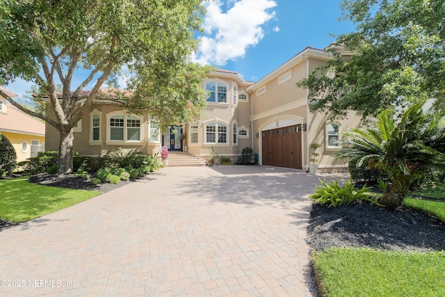 mediterranean / spanish-style house featuring a tile roof, stucco siding, a garage, and decorative driveway