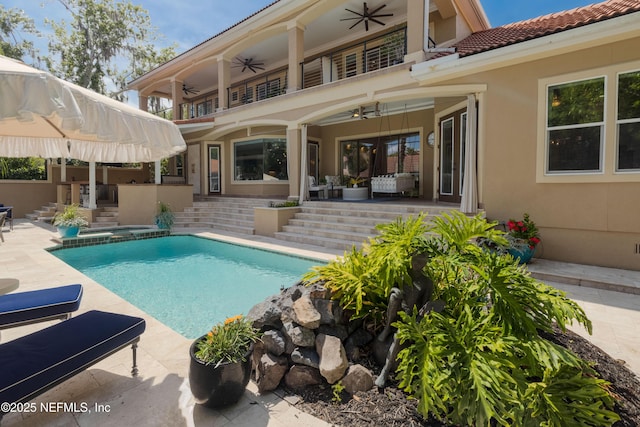 rear view of property featuring an outdoor pool, a patio area, a ceiling fan, and a balcony
