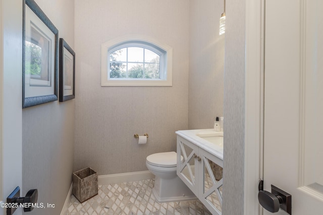 half bath with toilet, baseboards, and vanity