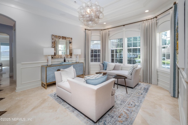 living room with a notable chandelier, wainscoting, a decorative wall, crown molding, and arched walkways