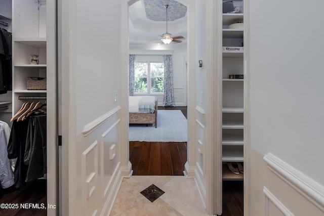 spacious closet featuring a tray ceiling, light wood-style flooring, and a ceiling fan