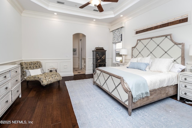 bedroom featuring a wainscoted wall, crown molding, wood-type flooring, arched walkways, and a tray ceiling