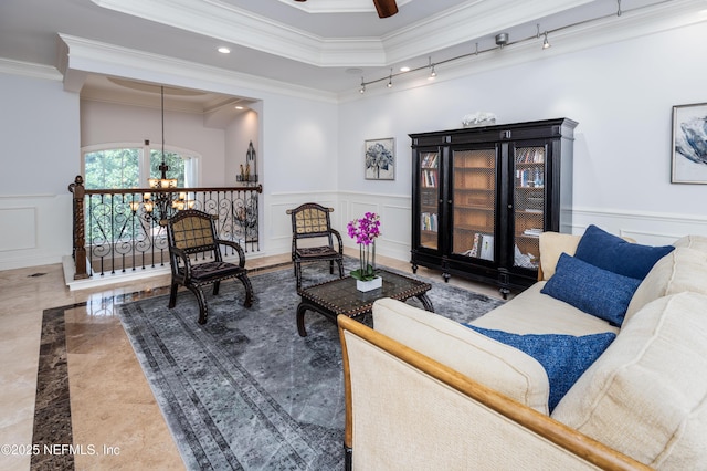 living area with wainscoting, crown molding, ceiling fan with notable chandelier, and a decorative wall