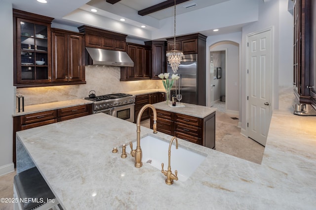 kitchen featuring under cabinet range hood, a sink, high quality appliances, decorative backsplash, and arched walkways