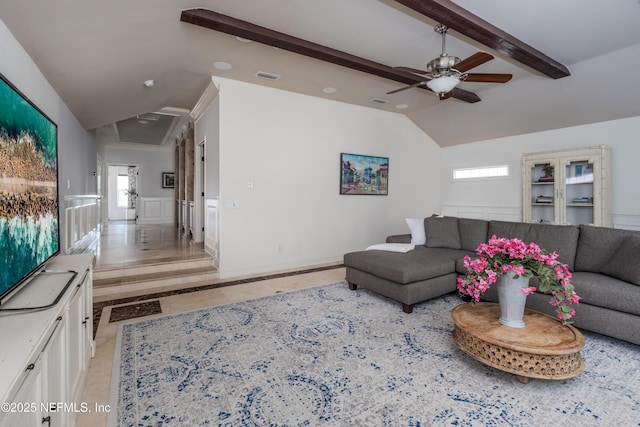 living area with a wainscoted wall, a healthy amount of sunlight, ceiling fan, and vaulted ceiling with beams