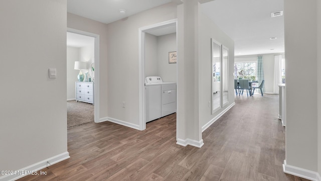 corridor with independent washer and dryer, visible vents, wood finished floors, and baseboards