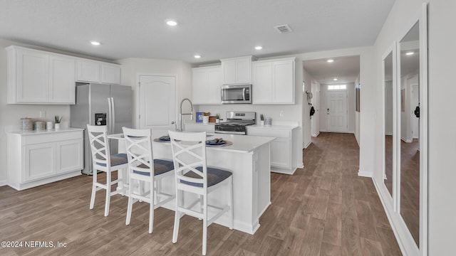 kitchen with a kitchen breakfast bar, a kitchen island with sink, visible vents, light wood-style flooring, and appliances with stainless steel finishes
